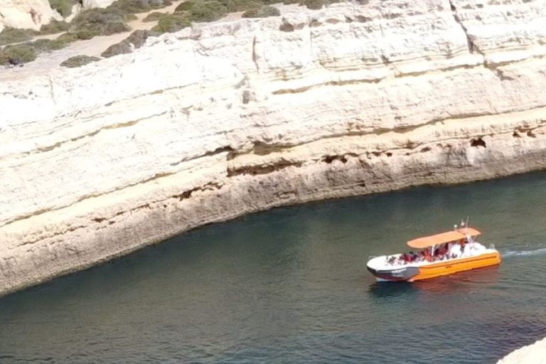 Aerial view of a cruise boat on turquoise water by the Algarve cliffs