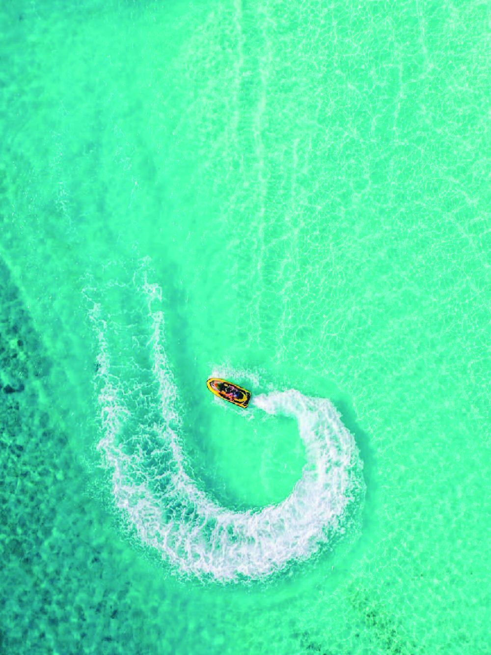 Aerial view of a jet ski carving a circle in turquoise water