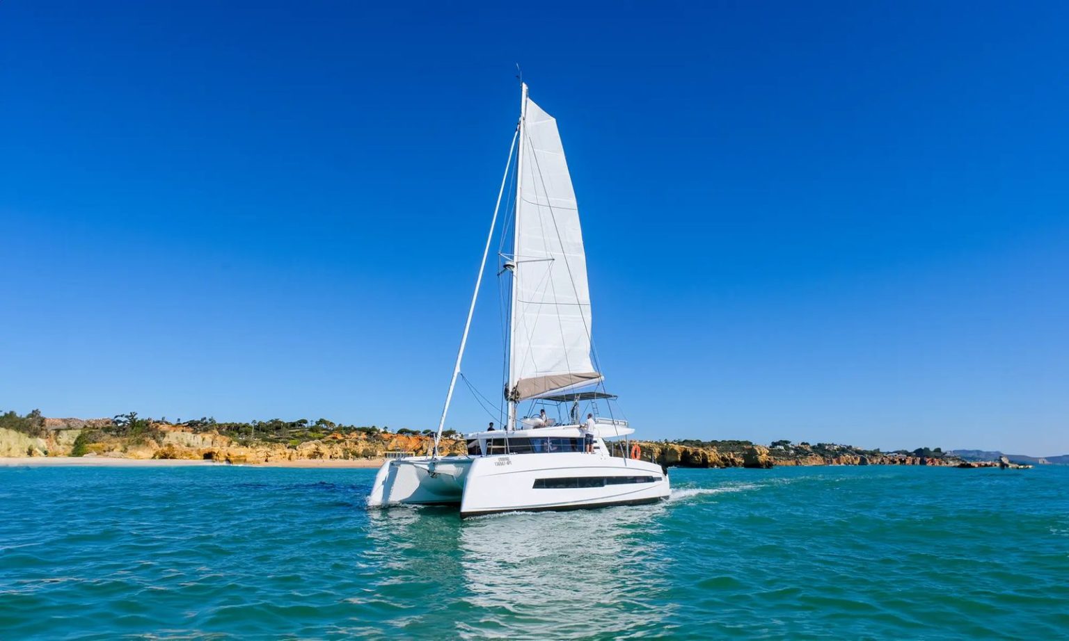 Private sailing catamaran cruising past a golden beach near Albufeira