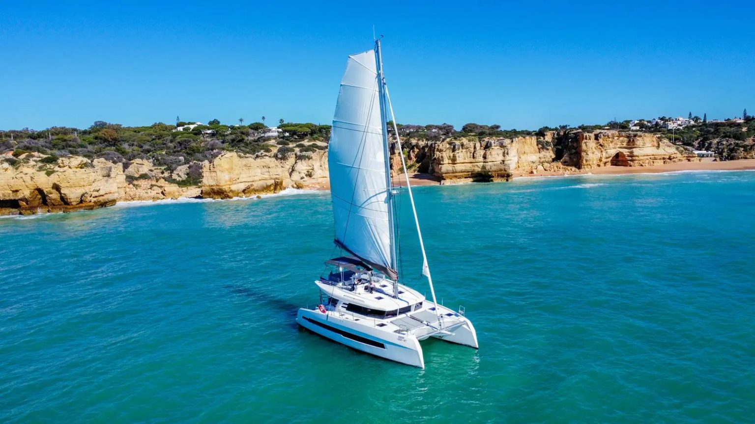 Private sailing catamaran in turquoise water below the Albufeira cliffs