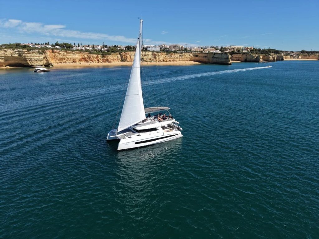 Aerial view of a sailing catamaran off the Algarve coast with cliffs and beaches