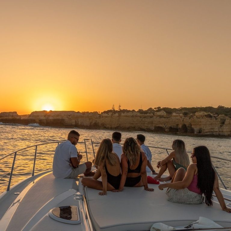 Guests watching the sunset over the cliffs from the bow of a private yacht
